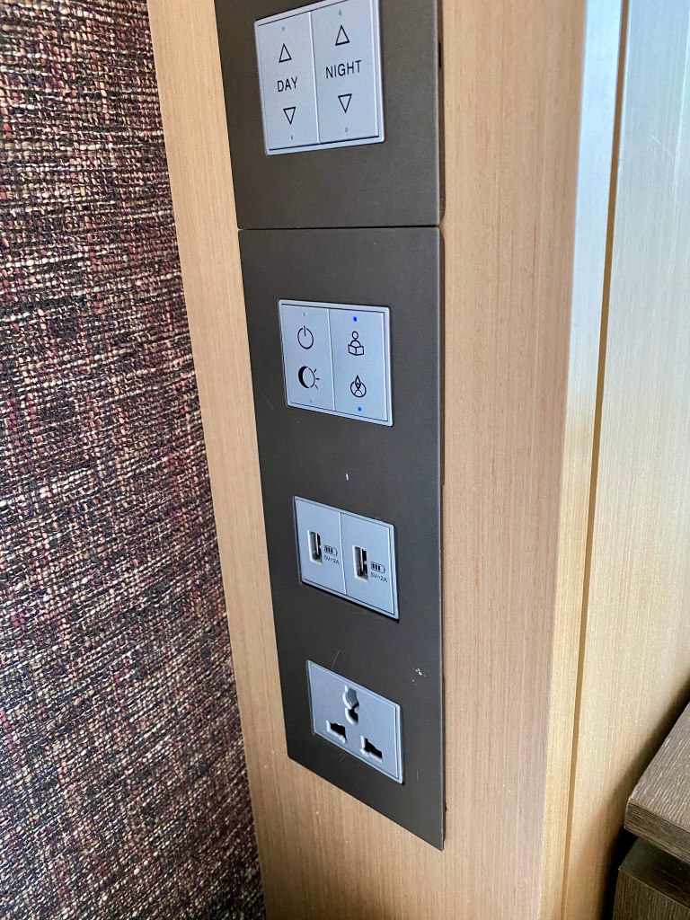 Control panels and power outlet is found on the wall by the bed