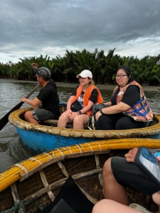 A group in a bamboo boat on a river, surrounded by green foliage under a cloudy sky.